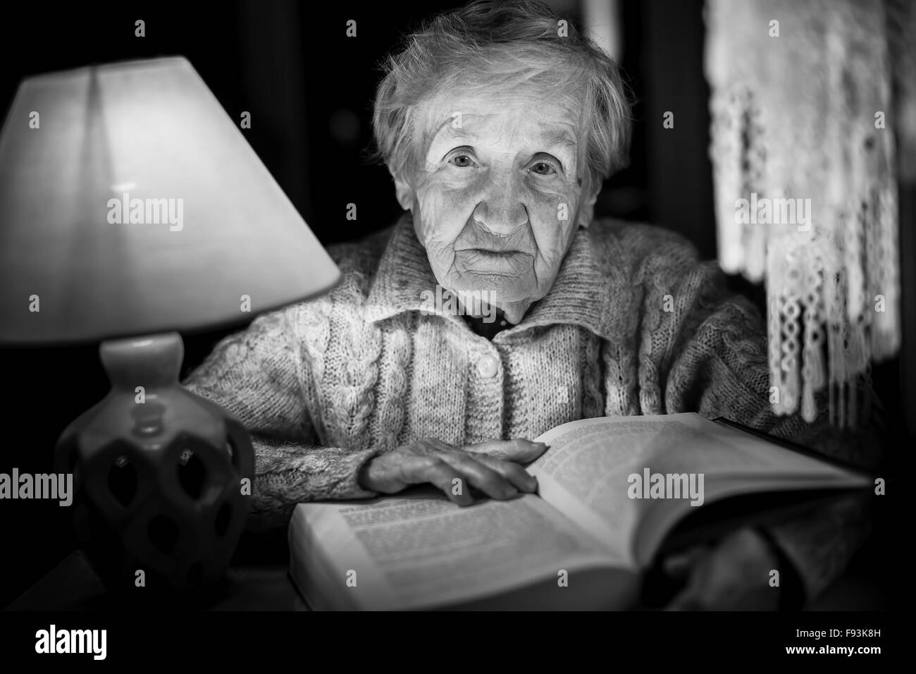 An elderly woman reading a book with night lamp. Black and white photo. Stock Photo