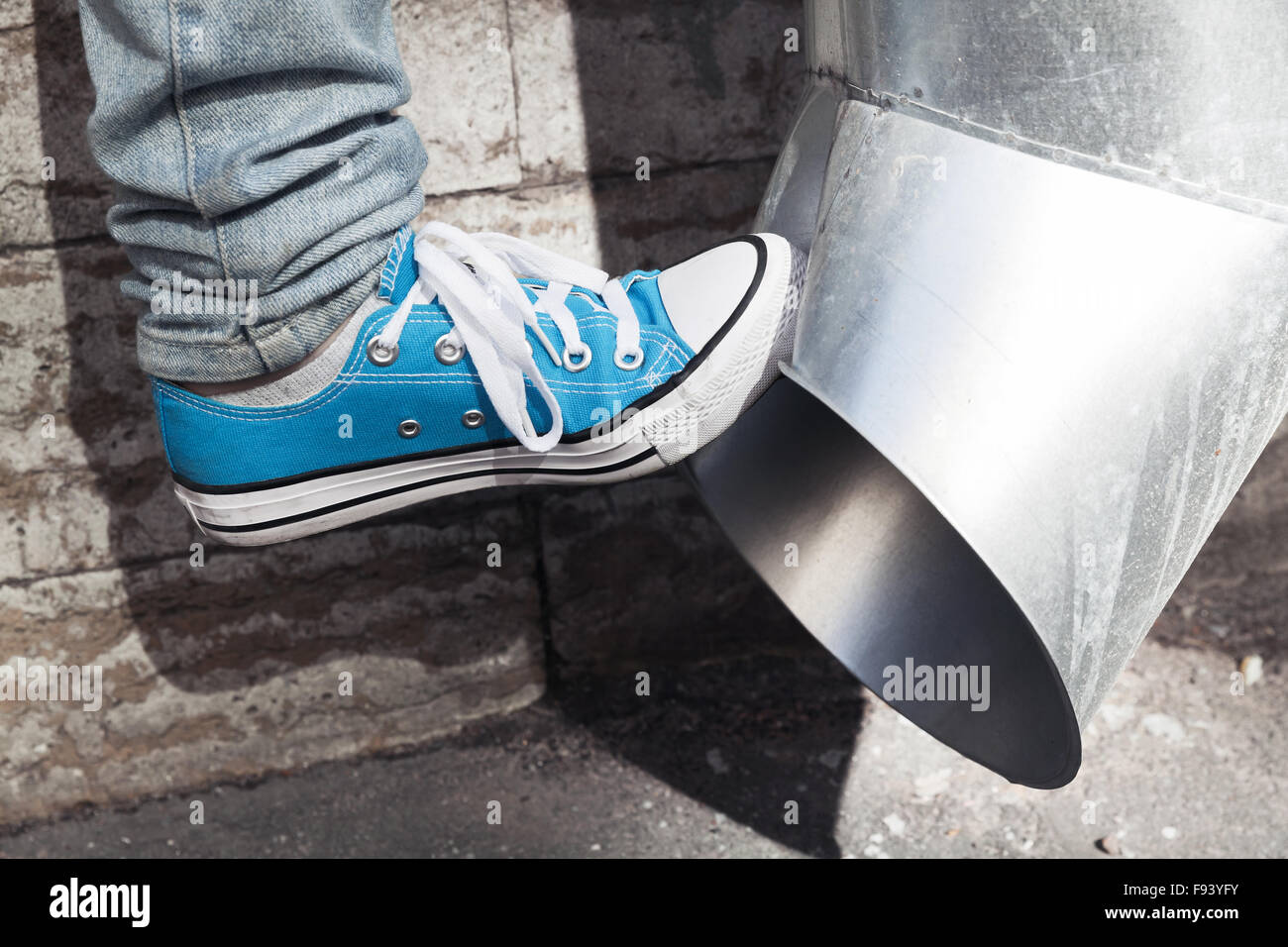 Teenager in blue sneakers kicks drainpipe, aggression concept Stock Photo