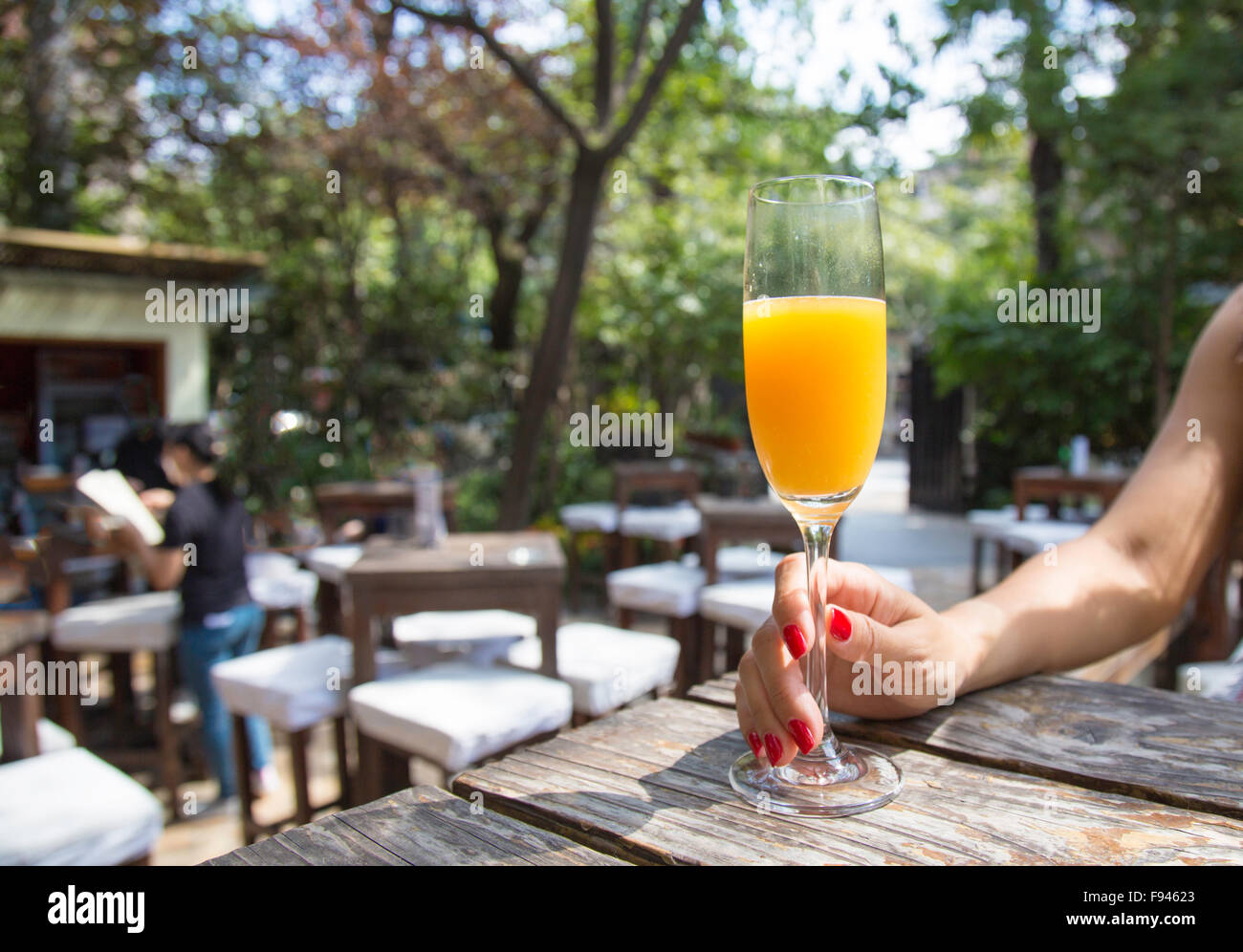 Woman's hand holding a glass of orange juice in beer-garden on a sunny day Stock Photo