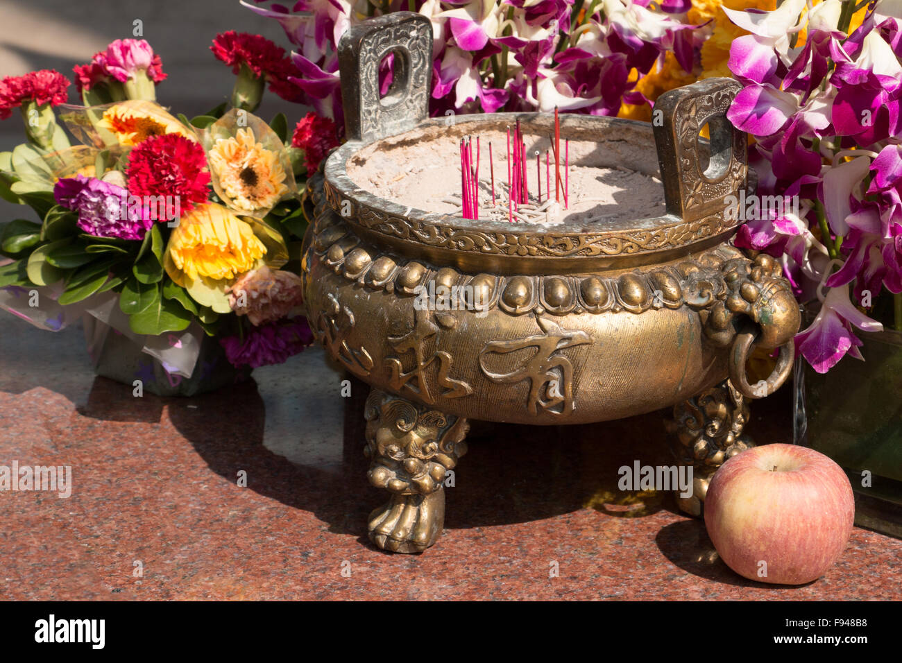 Chinese pot with incense sticks in front of a colored flower arrangement with an apple Stock Photo