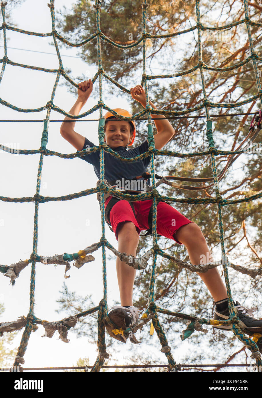 A boy wearing a safety harness and a helmet walking in a rope park ...