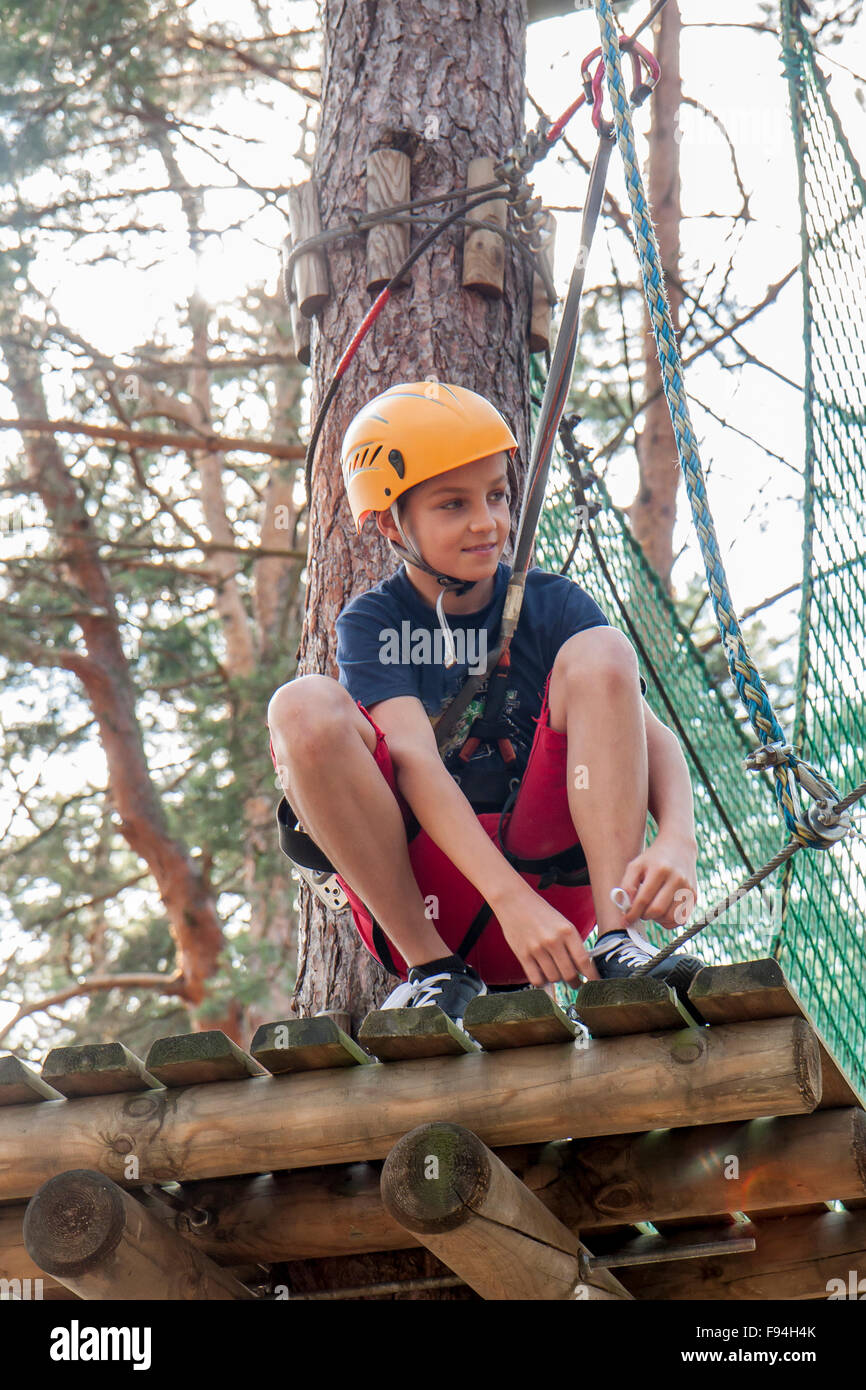 A boy wearing a safety harness and a helmet walking in a rope park ...