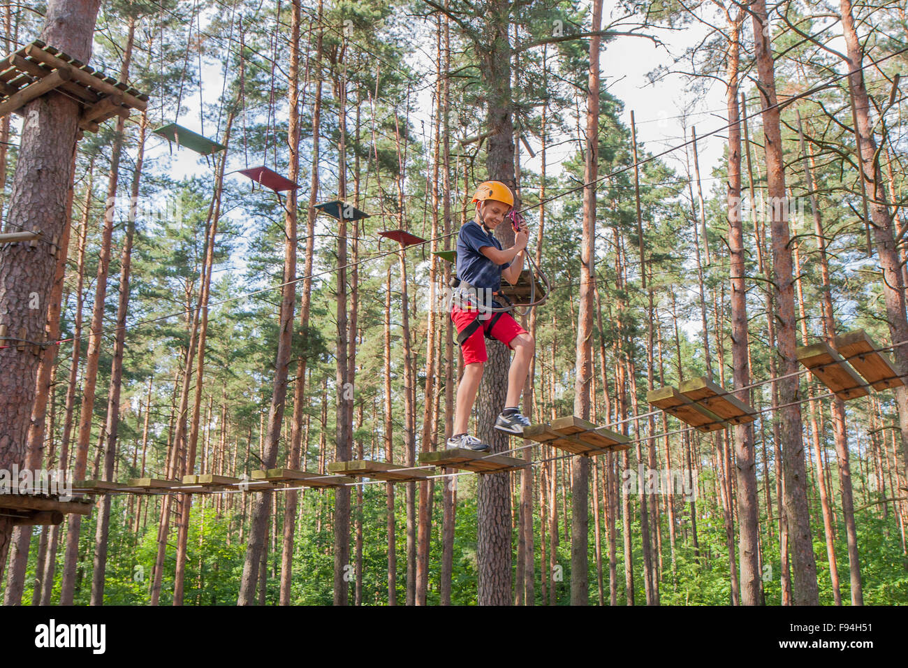 A boy wearing a safety harness and a helmet walking in a rope park ...