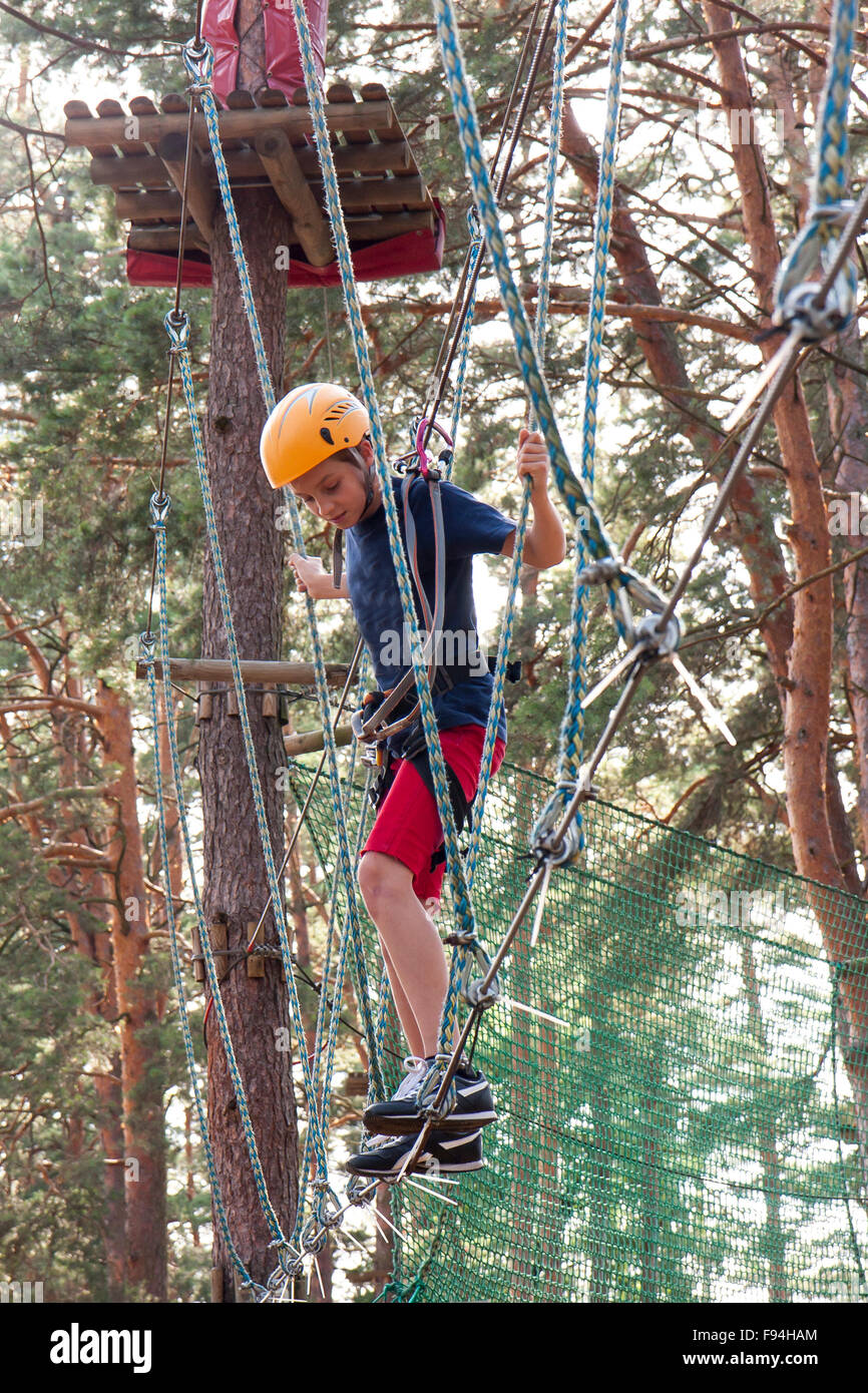 A boy wearing a safety harness and a helmet walking in a rope park ...