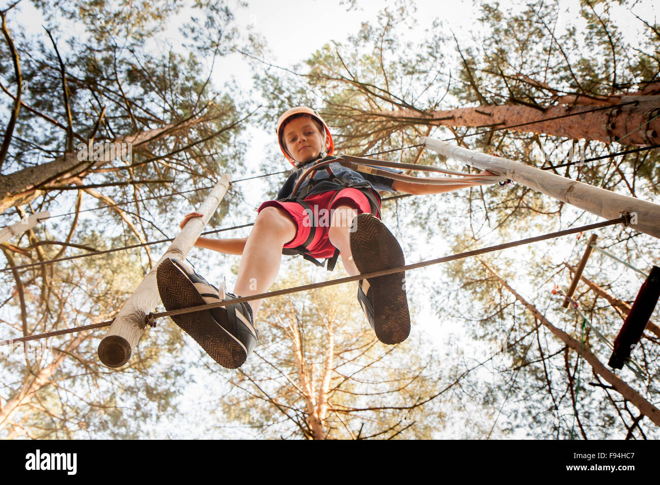 A boy wearing a safety harness and a helmet walking in a rope park ...