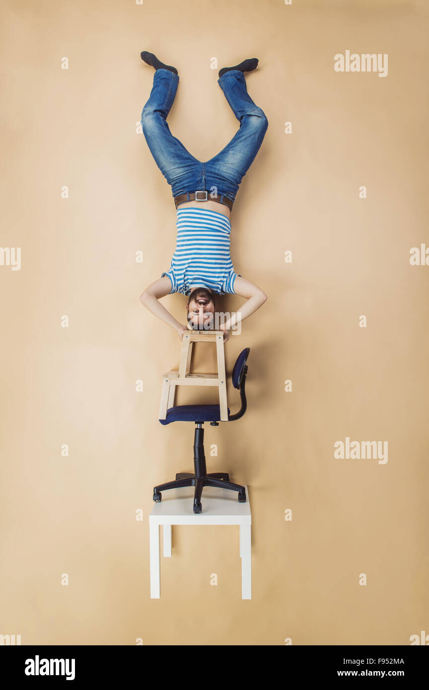 Man standing on a pile of chairs upside down. Studio shot on beige background. Stock Photo