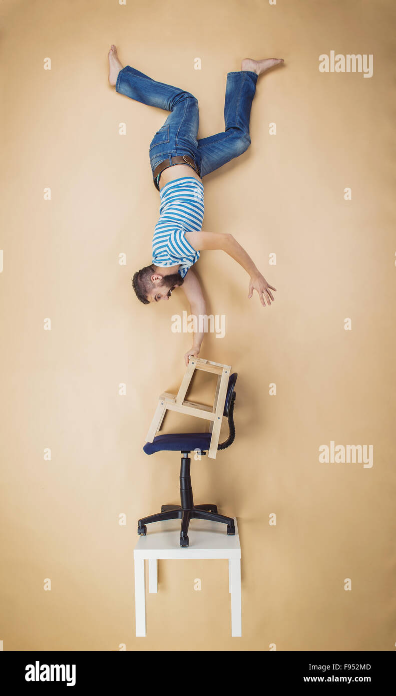 Man standing on a pile of chairs upside down. Studio shot on a beige background. Stock Photo