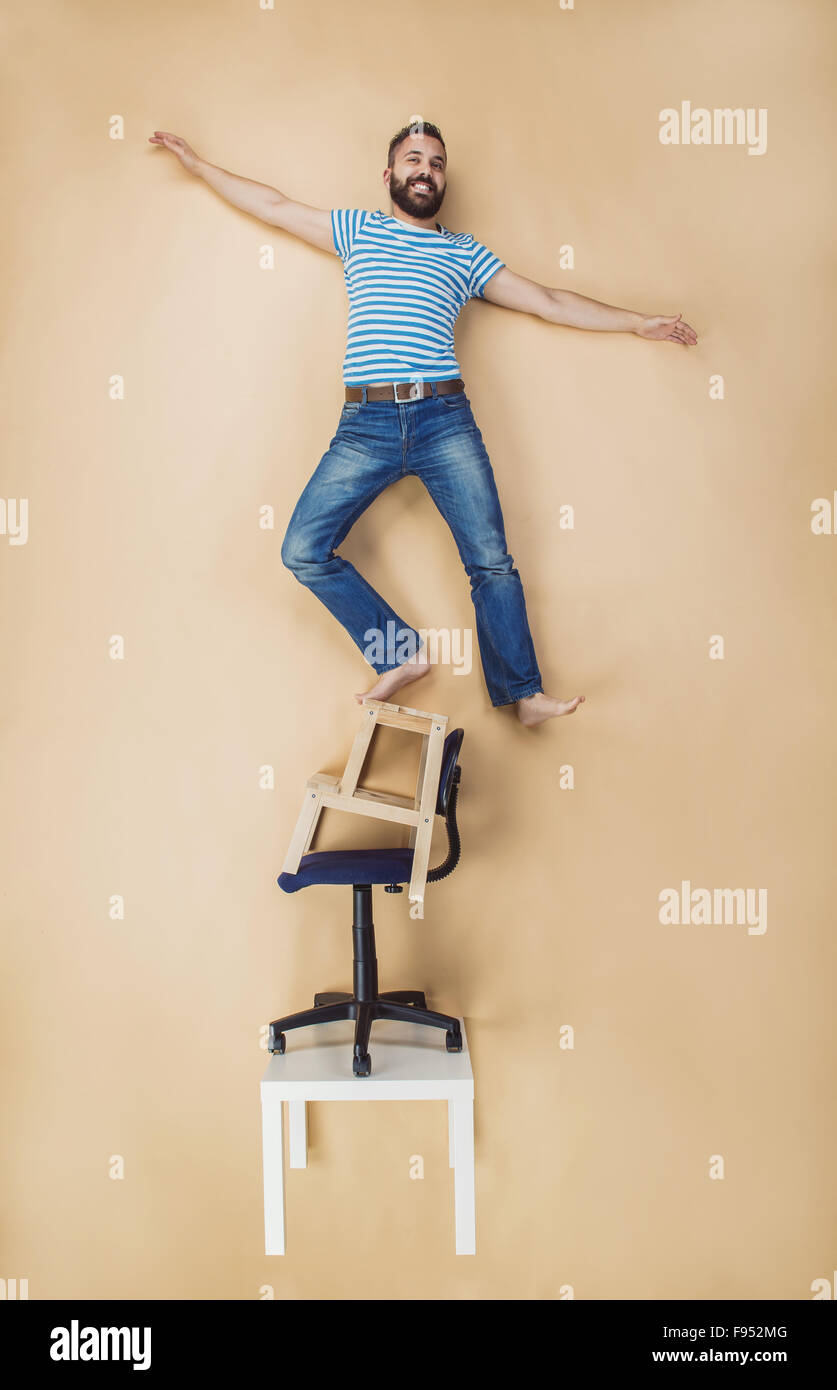 Man standing dangerously on a pile of chairs. Studio shot on a beige background. Stock Photo