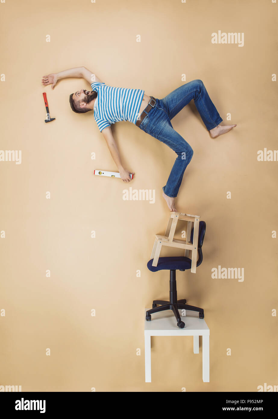 Handyman falling dangerously from a high pile of chairs. Studio shot on a beige background. Stock Photo