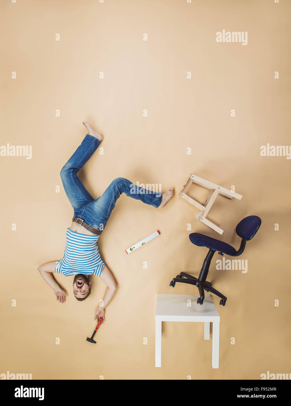 Handyman falling dangerously from a high pile of chairs. Studio shot on a beige background. Stock Photo