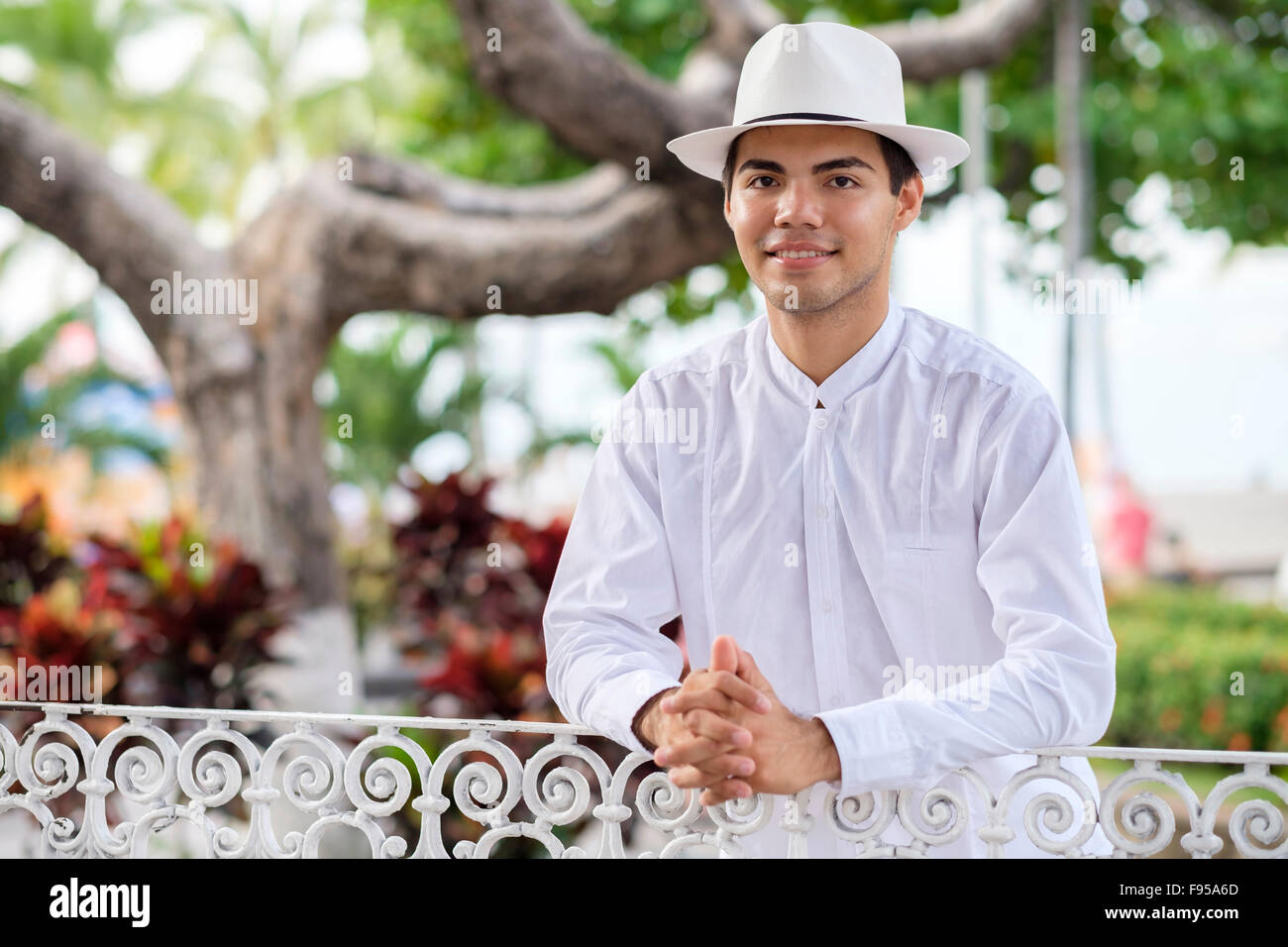 Young hispanic man in formal clothes, wearing white shirt, pants and hat, smiling at camera. Stock Photo