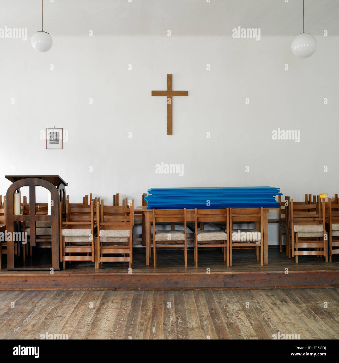 View of the interior of a church in Austria. Wood cross hanging on the wall and stacks of chairs in view. Stock Photo