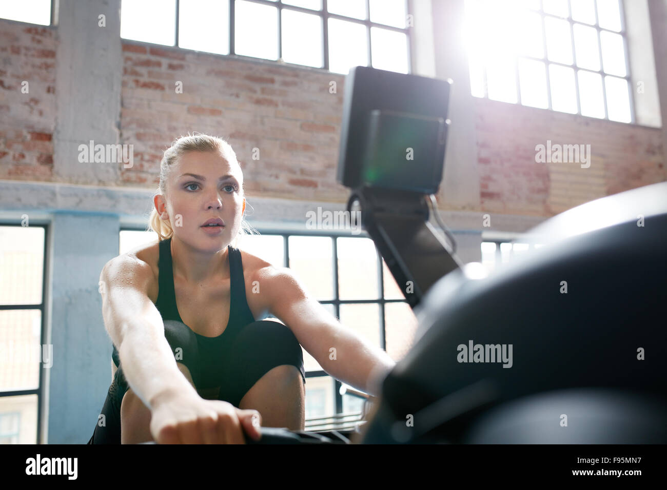 Fit young woman working out on a rowing machine at the gym. Caucasian female doing cardio exercise in fitness club. Stock Photo