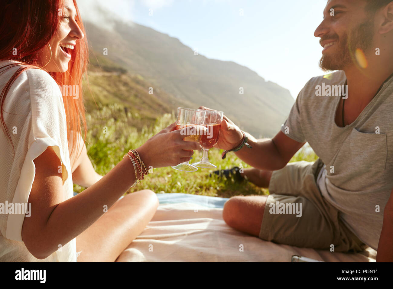 Shot of a cheerful young couple drinking wine and enjoying a picnic.  Young man with her girlfriend on vacation sitting on grass Stock Photo