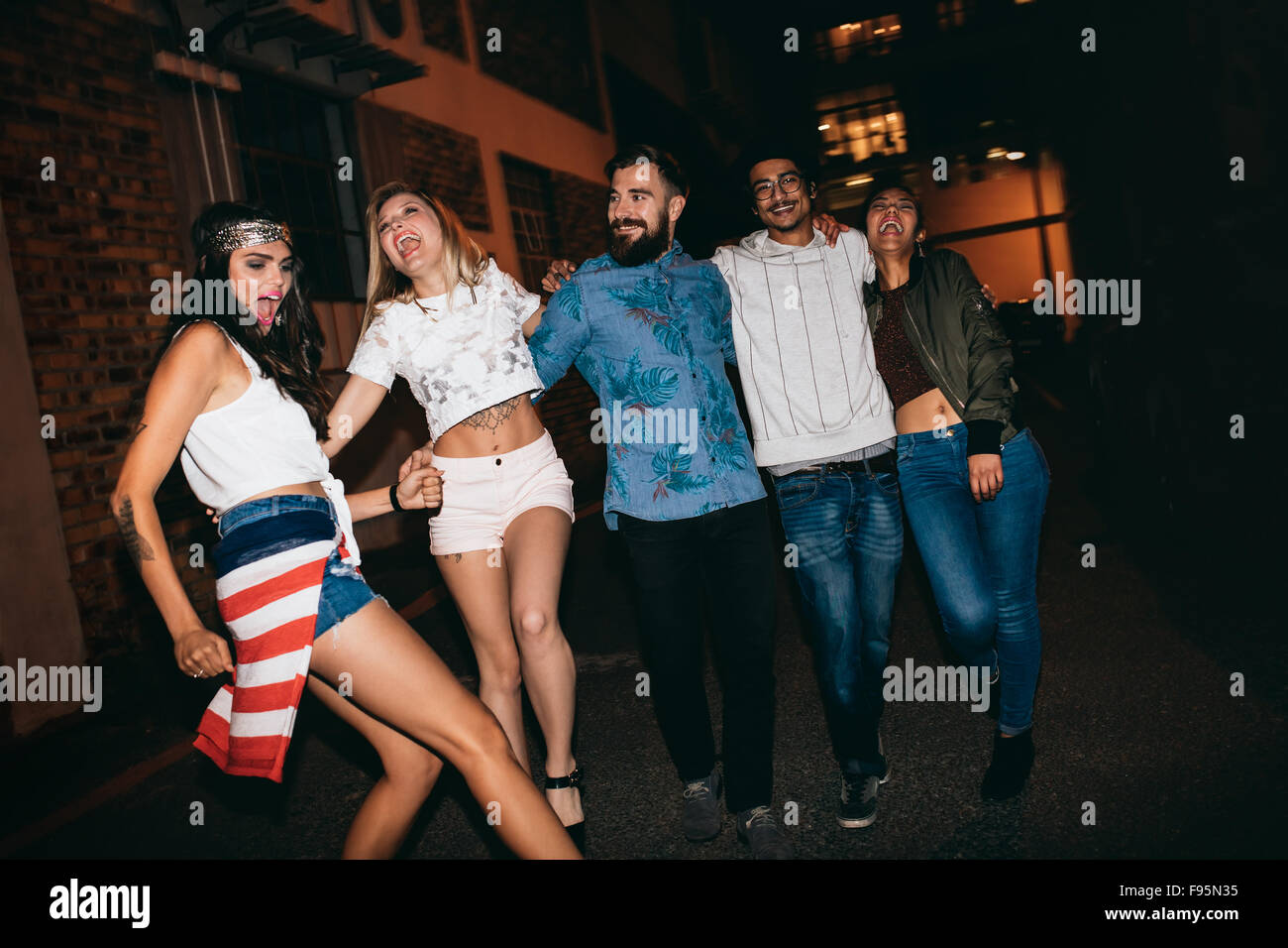 Cheerful young people walking together at night and having fun. Multiracial group of friends hanging out in evening. Stock Photo