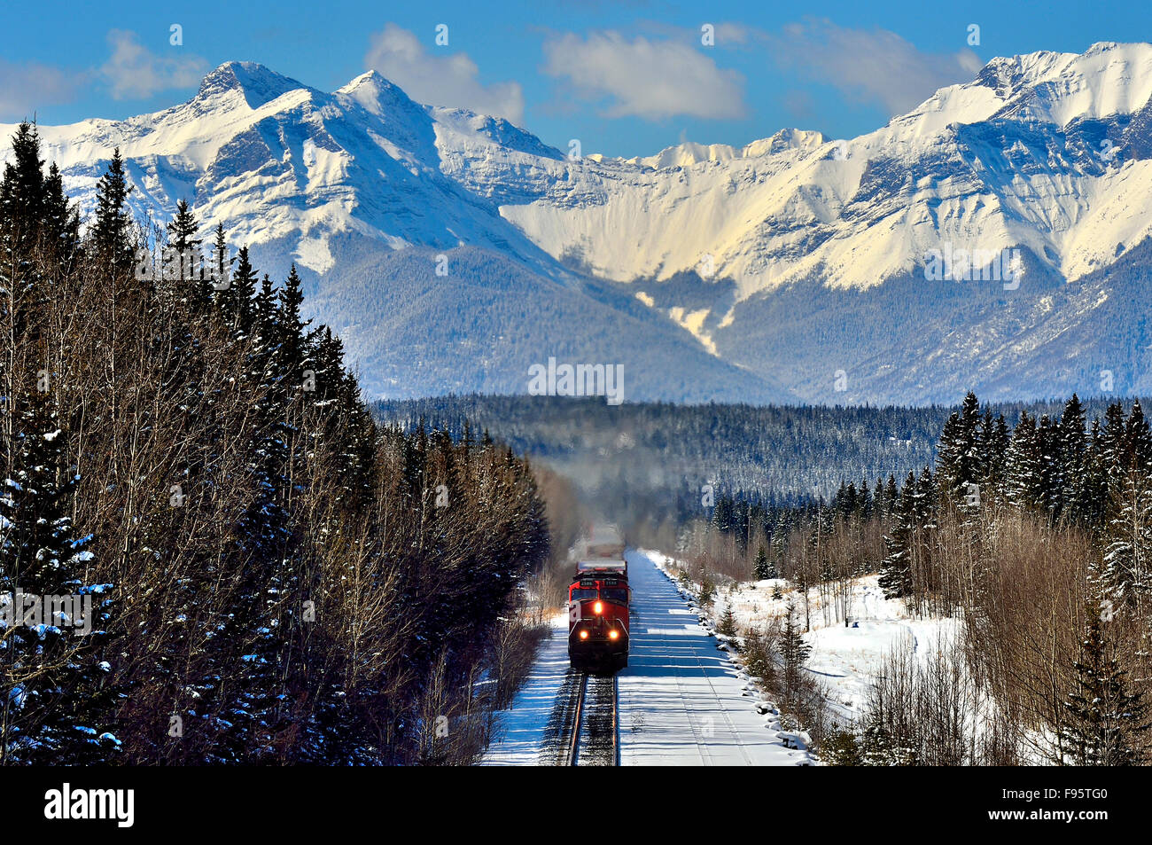 A horizontal image of a Canadian National freight train traveling through the snowcapped rocky mountains of Alberta Canada Stock Photo