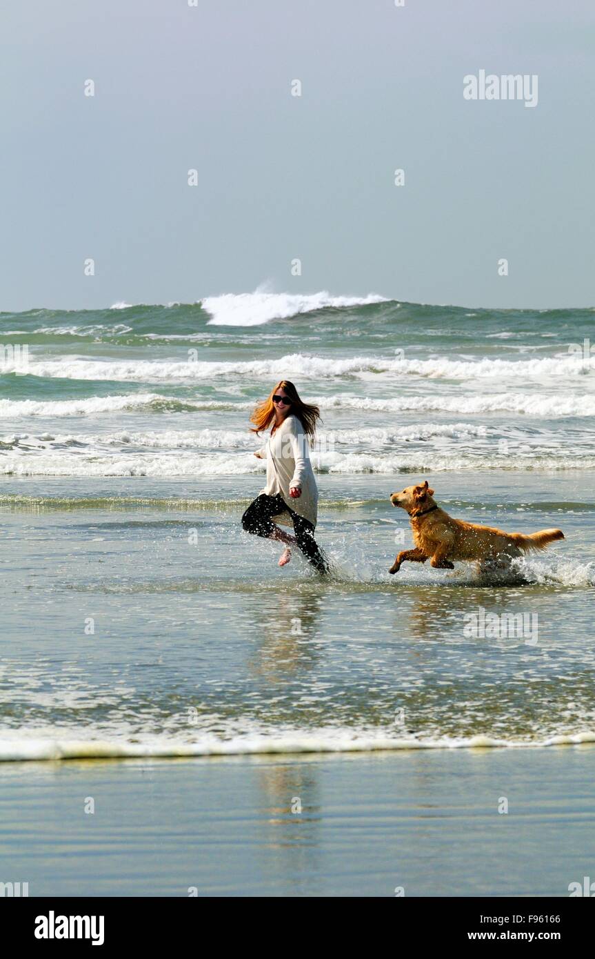 A young woman and her dog (a Golden Retriever) run with a ball in the surf on Chesterman Beach near Tofino, BC. Stock Photo