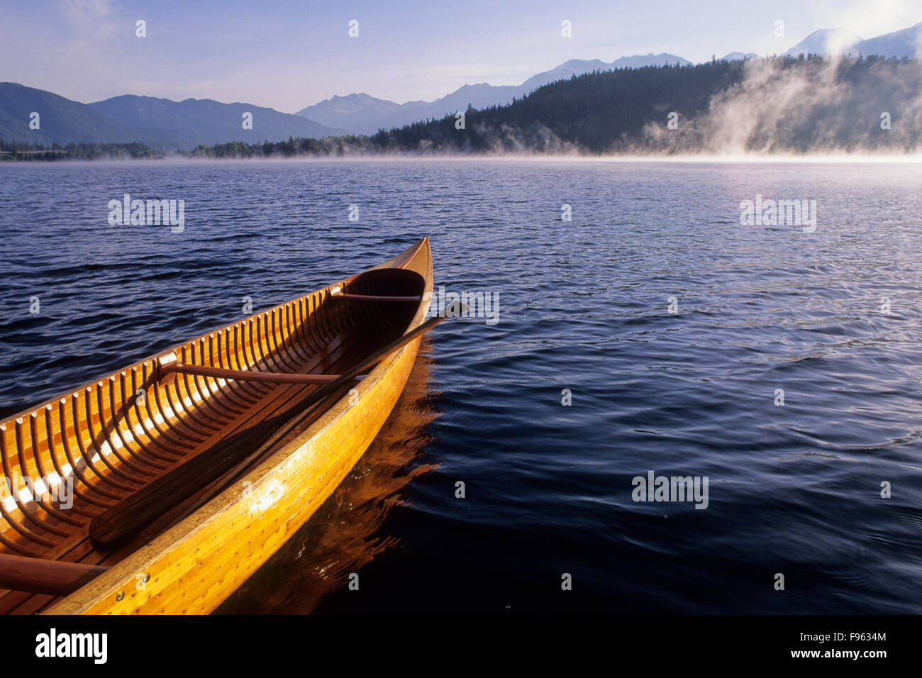 A cedar canoe waits for paddlers as the mist rises on Alta Lake in the autumn, Whistler, BC Canada Stock Photo