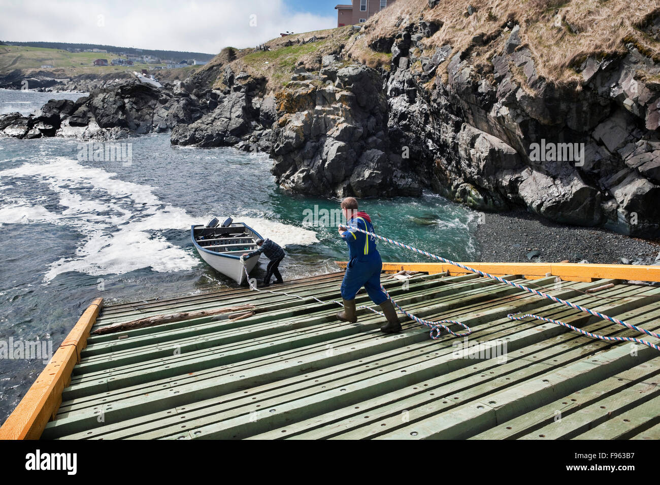 Two fishermen on a slipway (boat ramp) preparing their dory for an outing, Pouch cove, Newfoundland, Canada Stock Photo