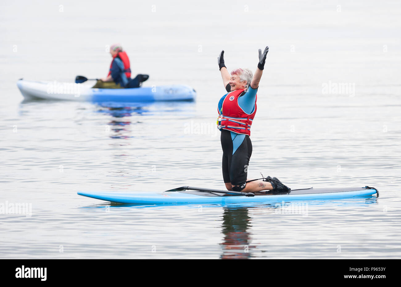 A senior woman stretches while paddle boarding at Stories Beach near