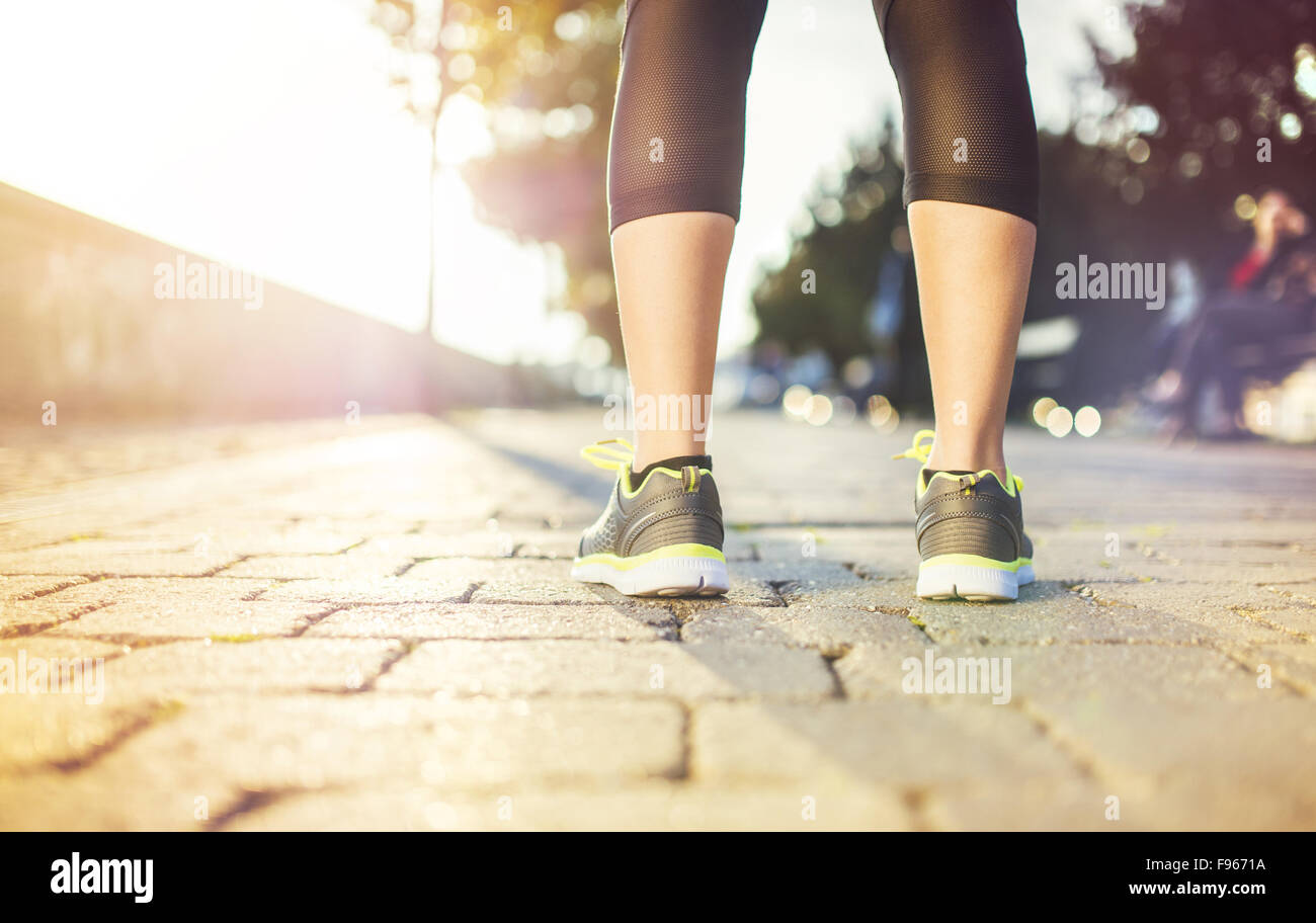 Female runner running on tiled pavement in city quay, closeup on shoes