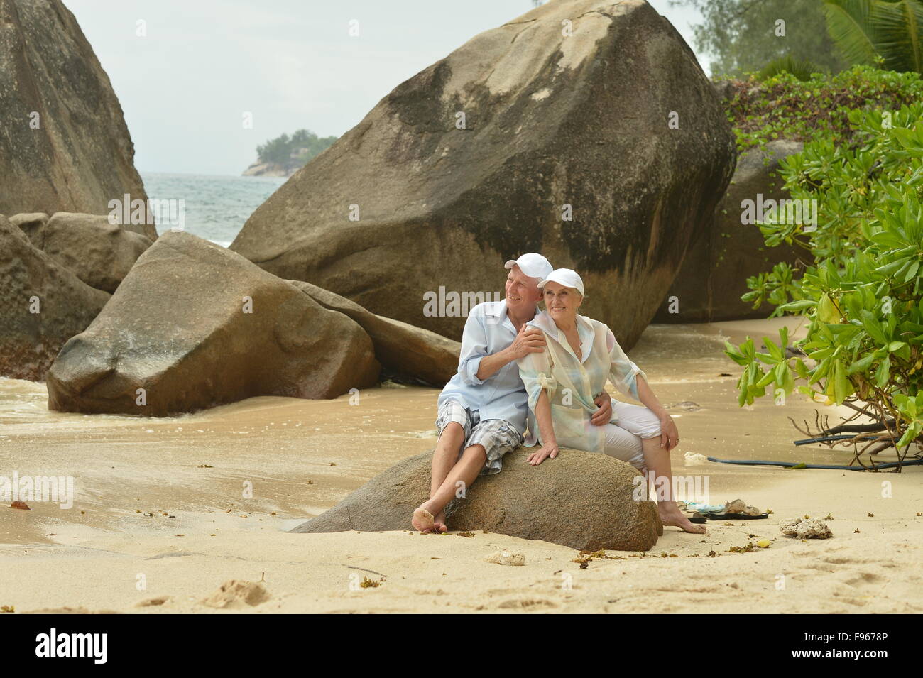 Happy elderly couple sitting on a large rock on the beach Stock Photo