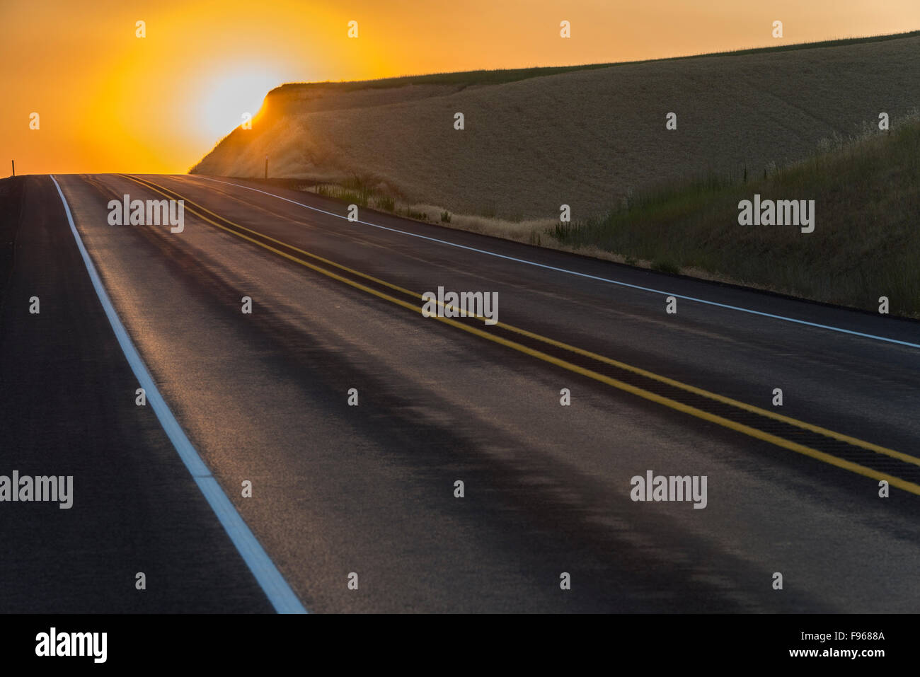 Sun rising behind a hill on top of a road near town of Colfax, Washington, U.S.A Stock Photo