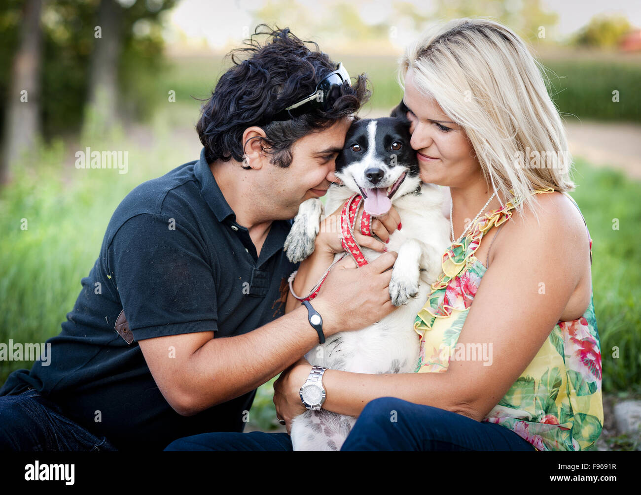 Happy young couple is playing their two dog in green nature Stock Photo ...