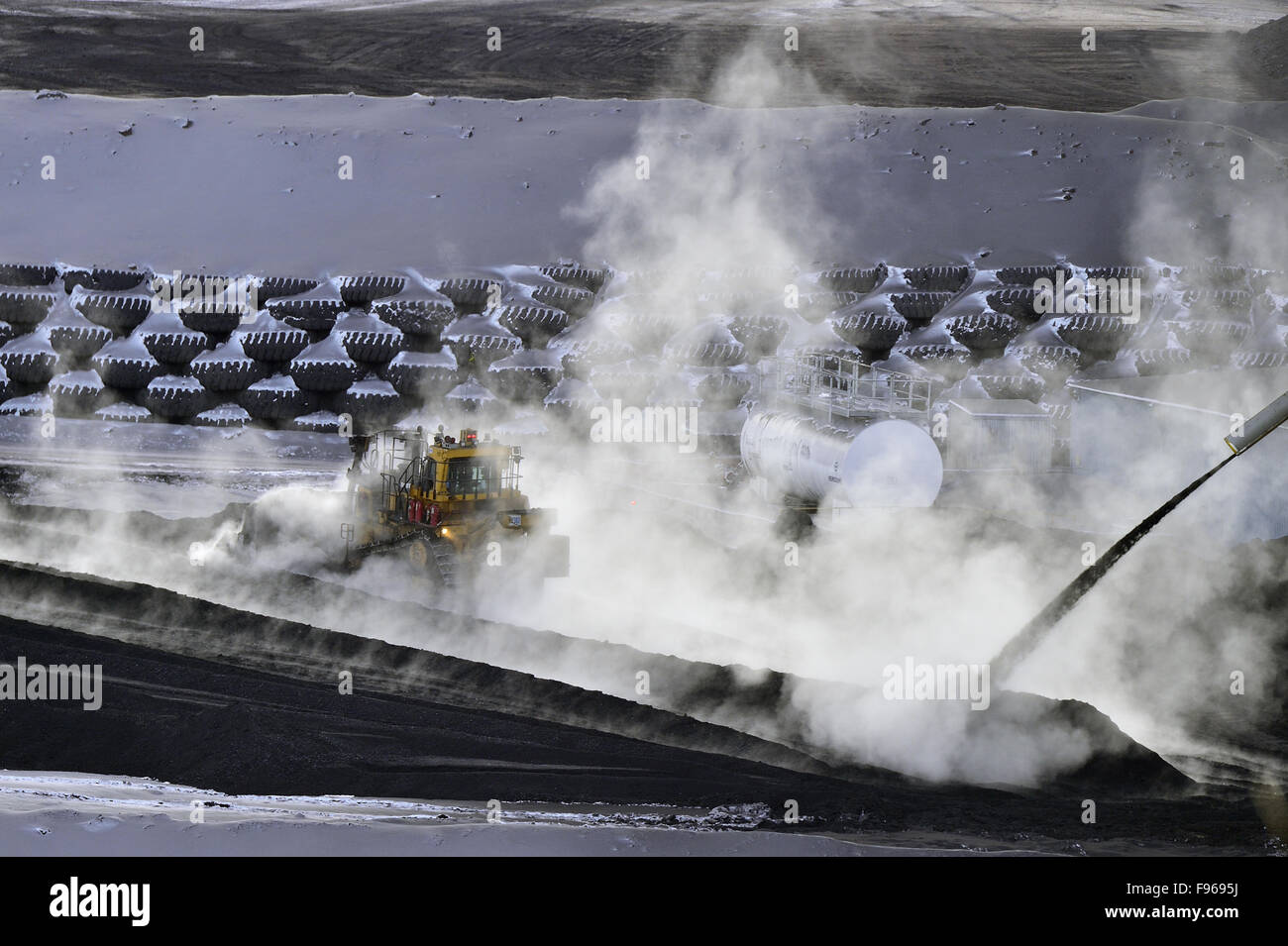 Steam from the hot coal surrounds the bull dozer as it pushes the fresh coal product into a pile at the Luscar coal mine's Stock Photo