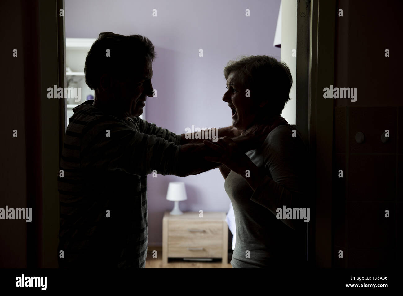 Silhouette of mature couple fighting, the man is physically abusing woman. Woman is victim of domestic violence Stock Photo