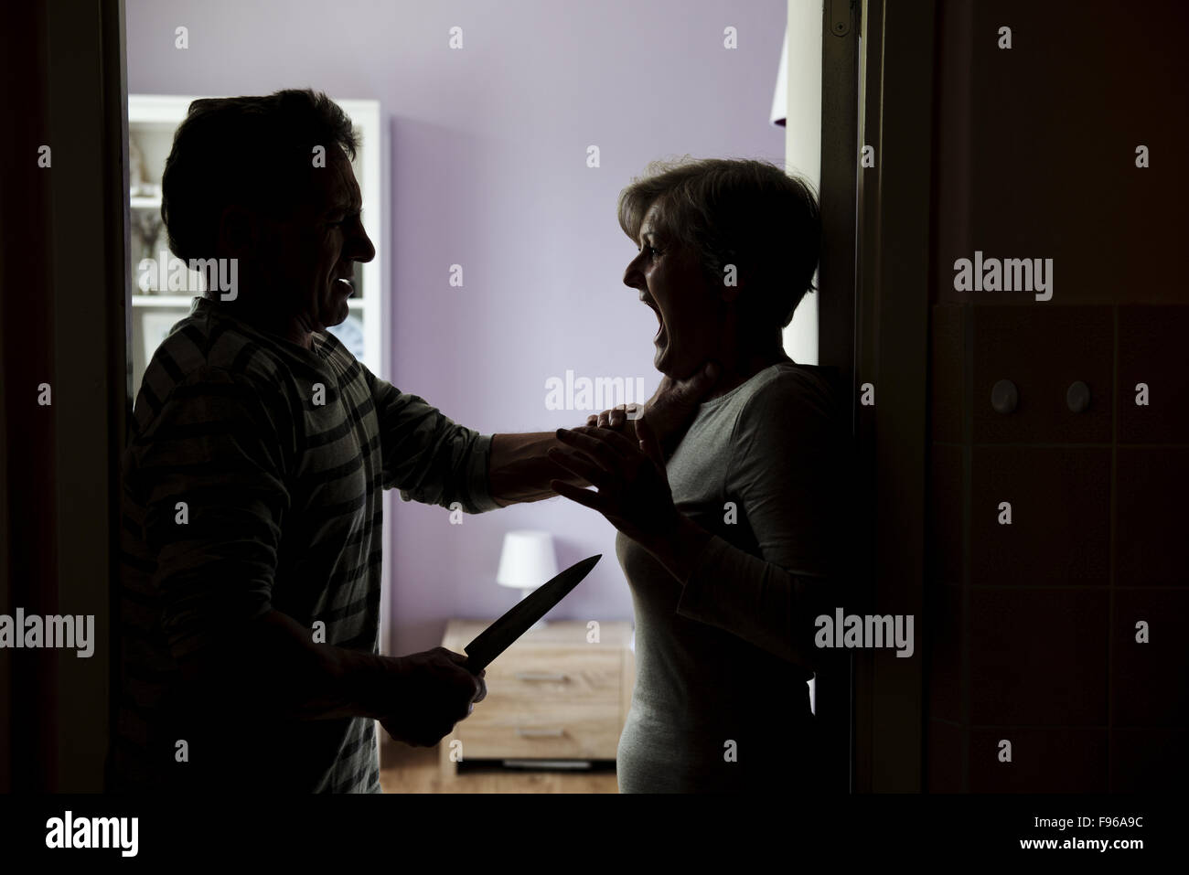 Silhouette of mature couple fighting, the man is attacking woman with knife. Woman is victim of domestic violence Stock Photo