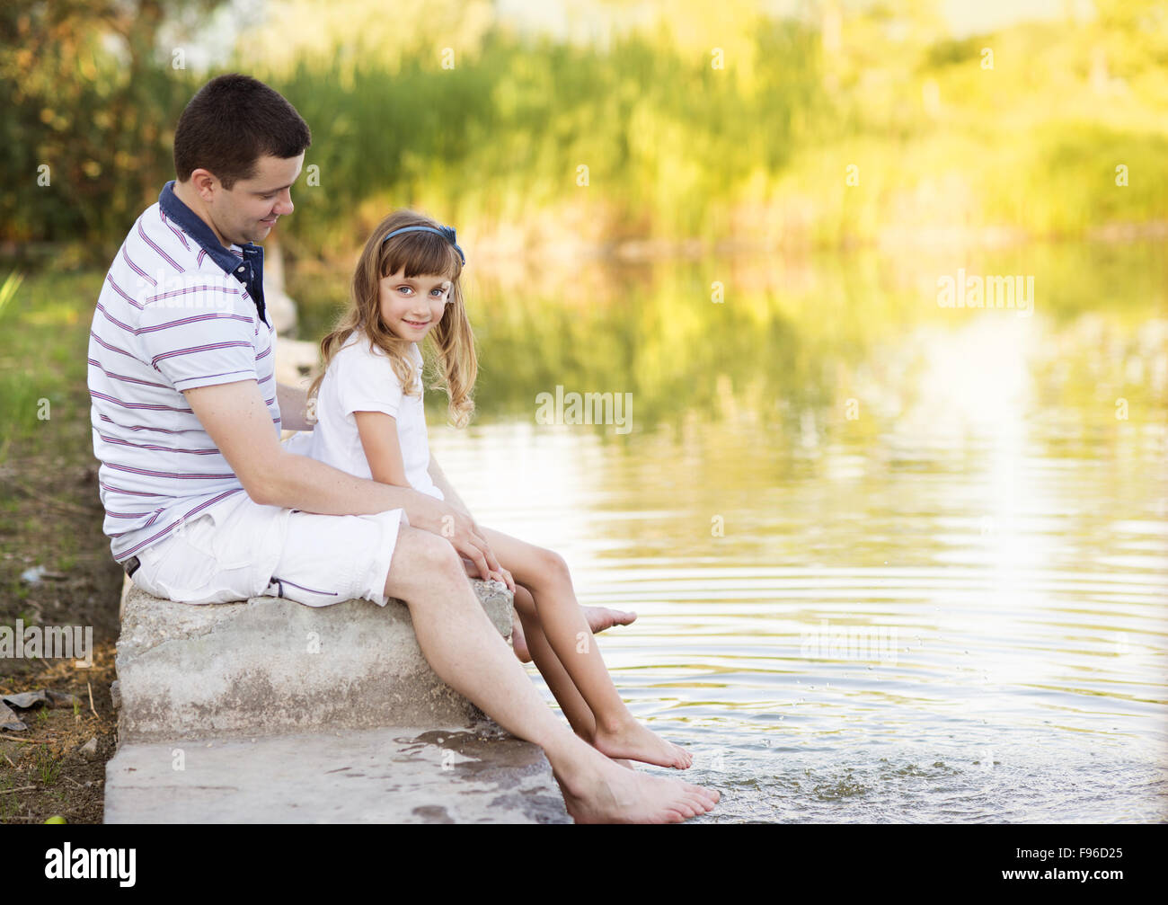 Happy young father sitting by the lake with his little daughter Stock Photo