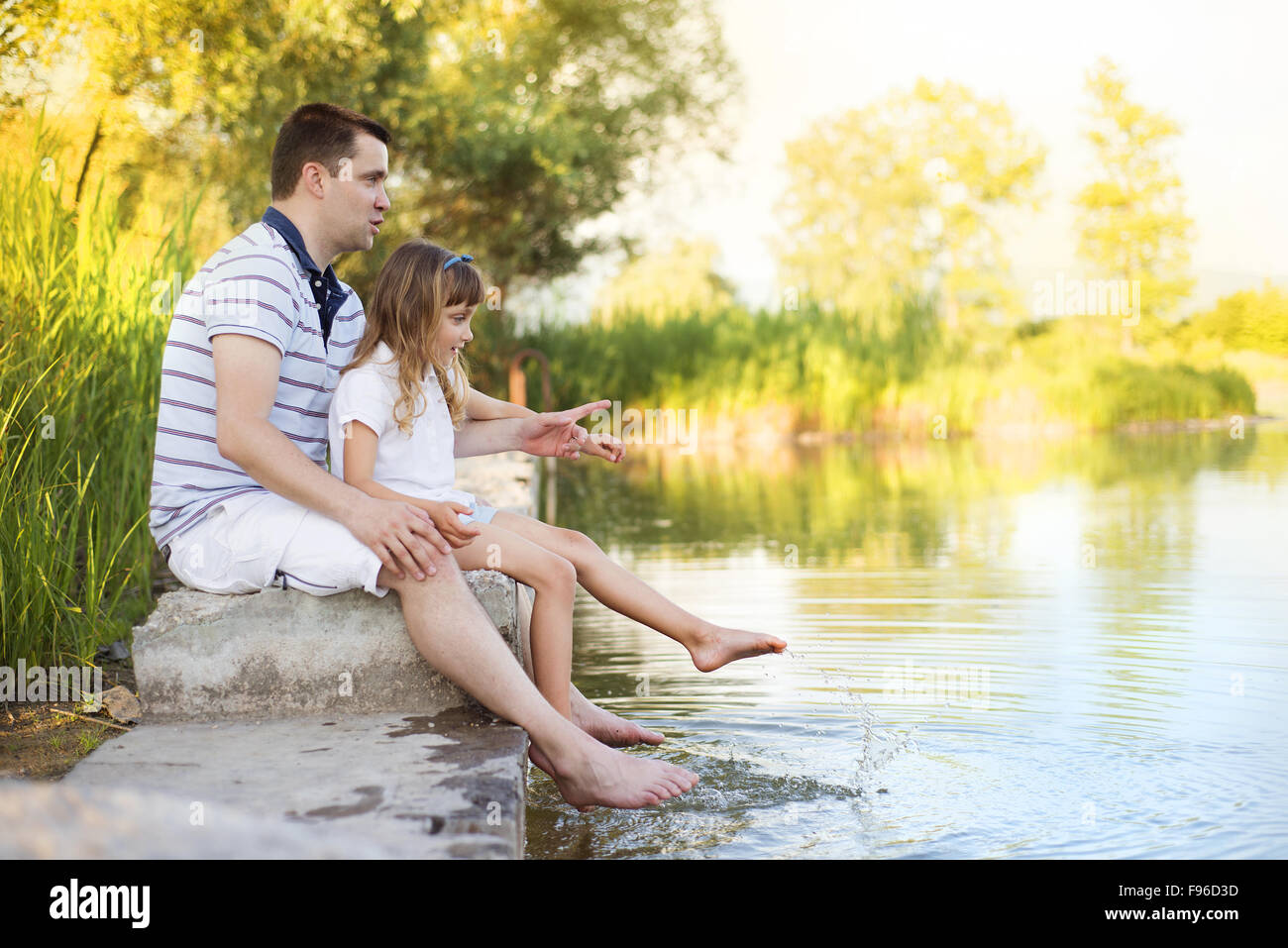 Happy young father sitting by the lake with his little daughter Stock Photo