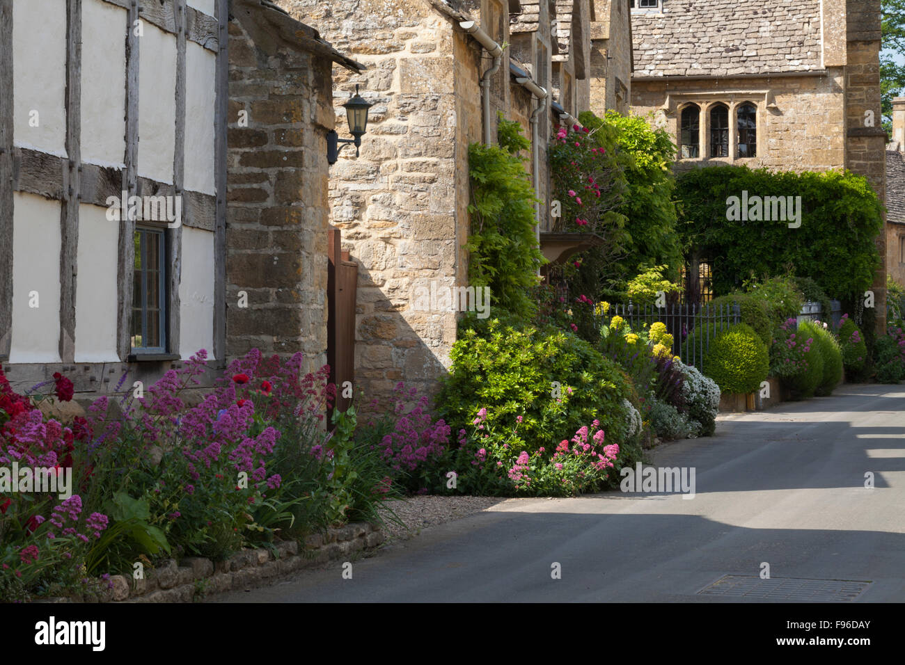 Colourful summer flowers and fine stone houses line a quiet street in the Cotswolds village of Stanton, Gloucestershire, England Stock Photo