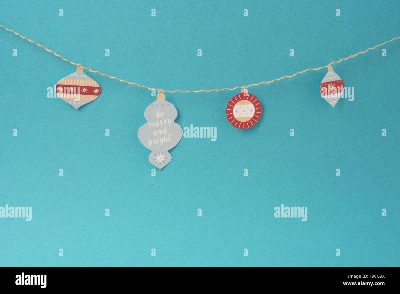 Christmas paper decoration, simple handmade Xmas label ornaments hanging on string over empty blue background with blank space. Stock Photo