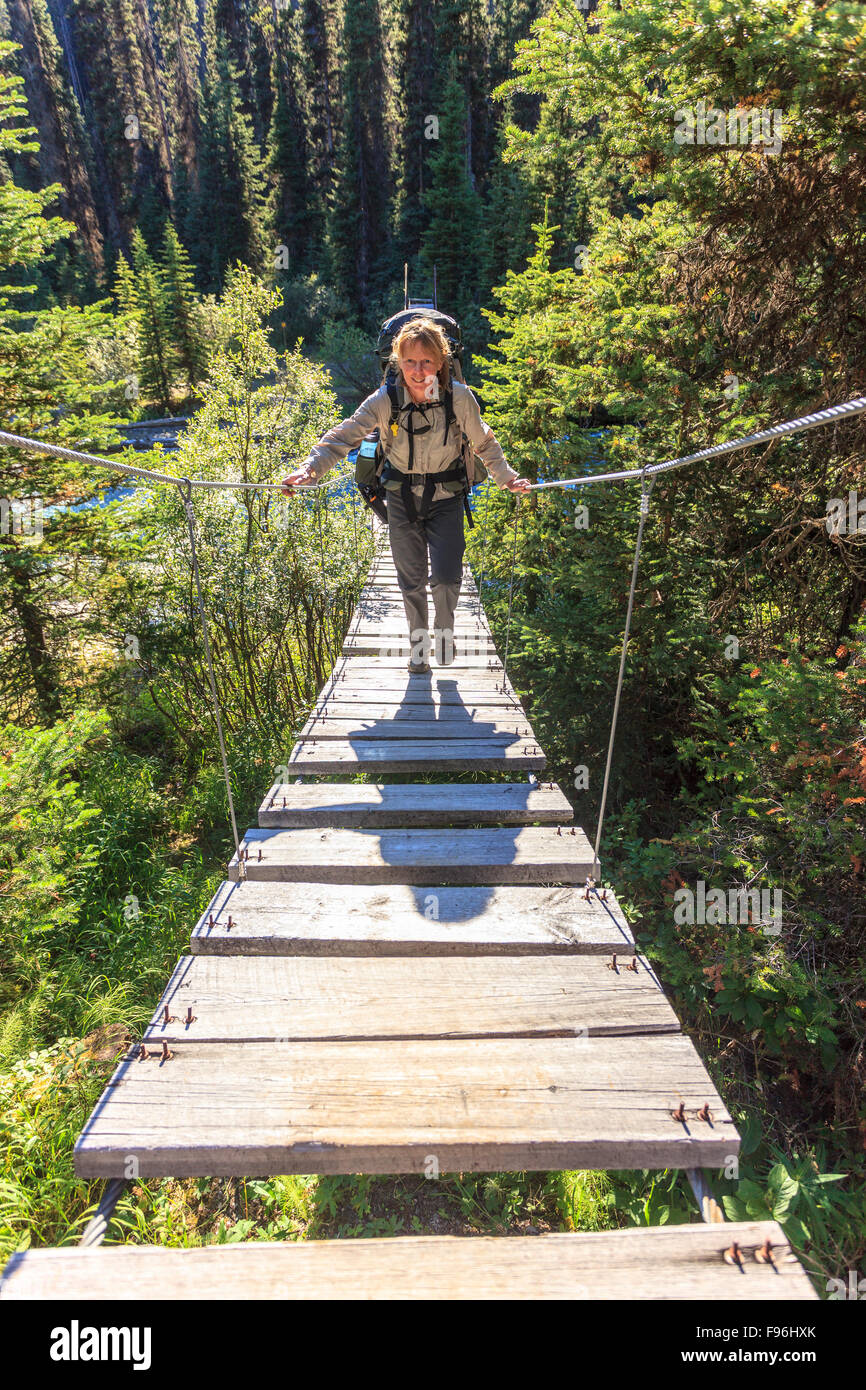 A back packer crosses a suspension bridge over a river in Kootenay National Park, British Columbia Canada. Model Released Stock Photo