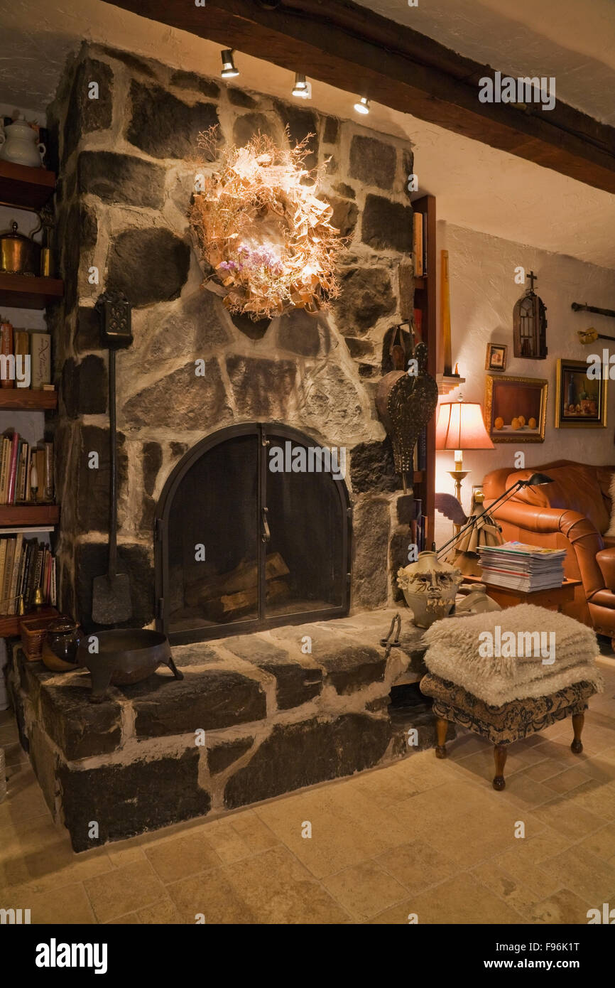 Flagstone fireplace next to brown leather sofa in the reading room inside an old 1809 cottage style residential home, Quebec, Stock Photo