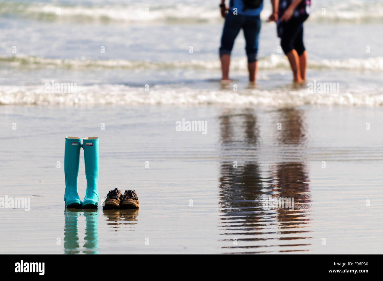 A pair of gumboots and a pair of shoes sit on the sand while their owners get their feet wet on Chesterman Beach in Tofino, Stock Photo