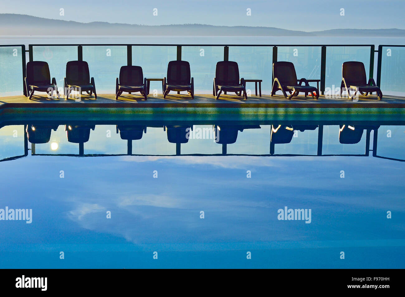 A horizontal image of  a line of chairs at an outdoor swimming pool at vacation resort on Vancouver Island B.C. Canada. Stock Photo