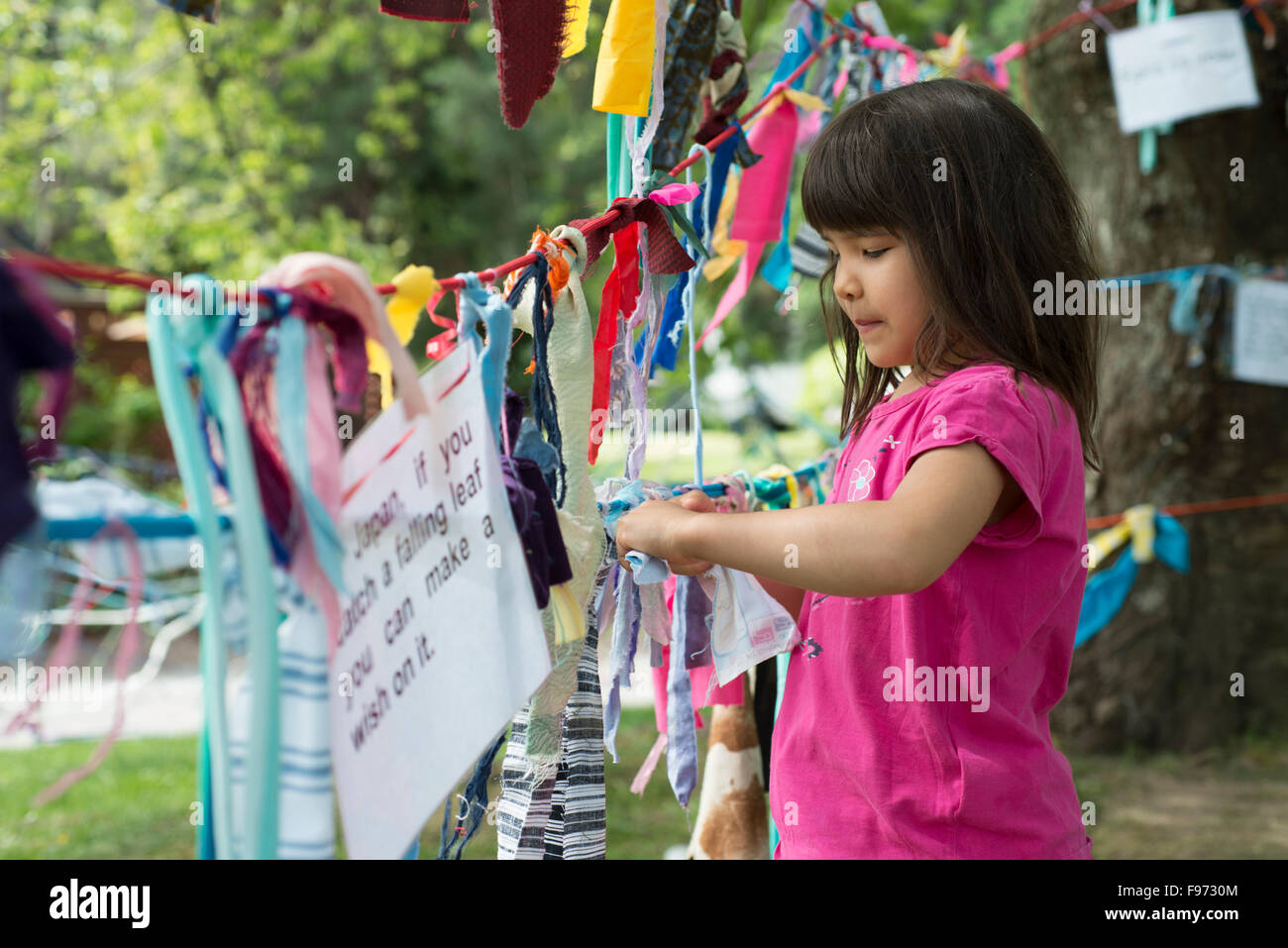 Young girl ties fabric on a wishing tree at the Vancouver International Children's Festival, Granville Island, Vancouver, Stock Photo