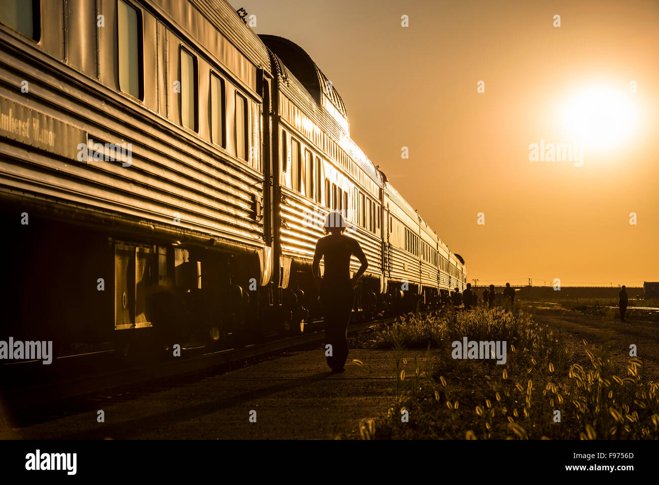 Passengers walking beside stopped passenger train at sunset. Stock Photo