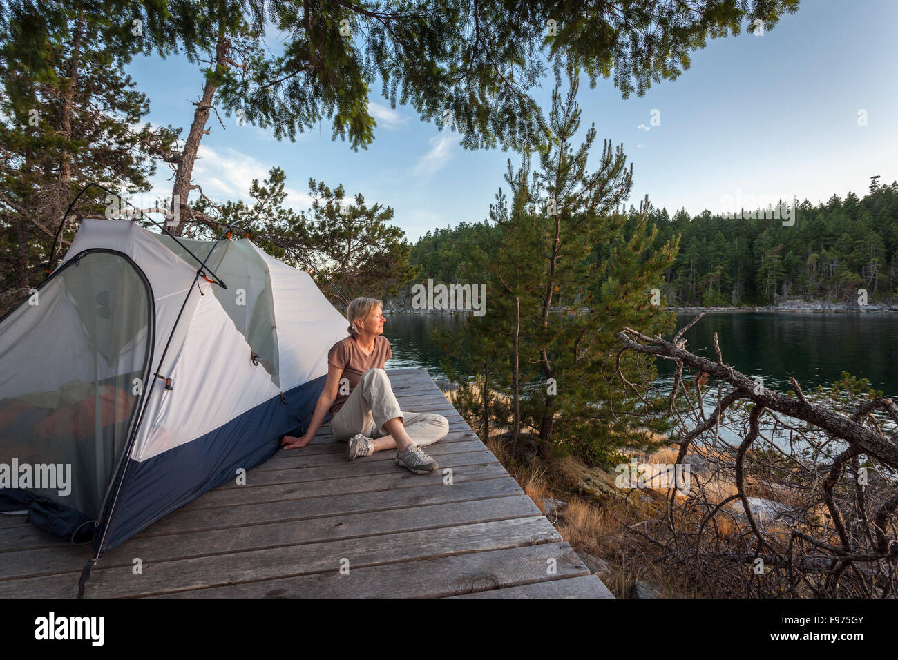 A camper relaxes on a platform next to her tent at dusk. West Curme Island, Desolation Sound Marine Park, British Columbia, Stock Photo