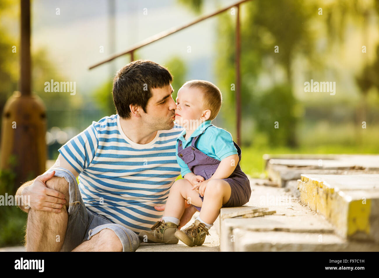Outdoor portrait of young father kissing his little son Stock Photo