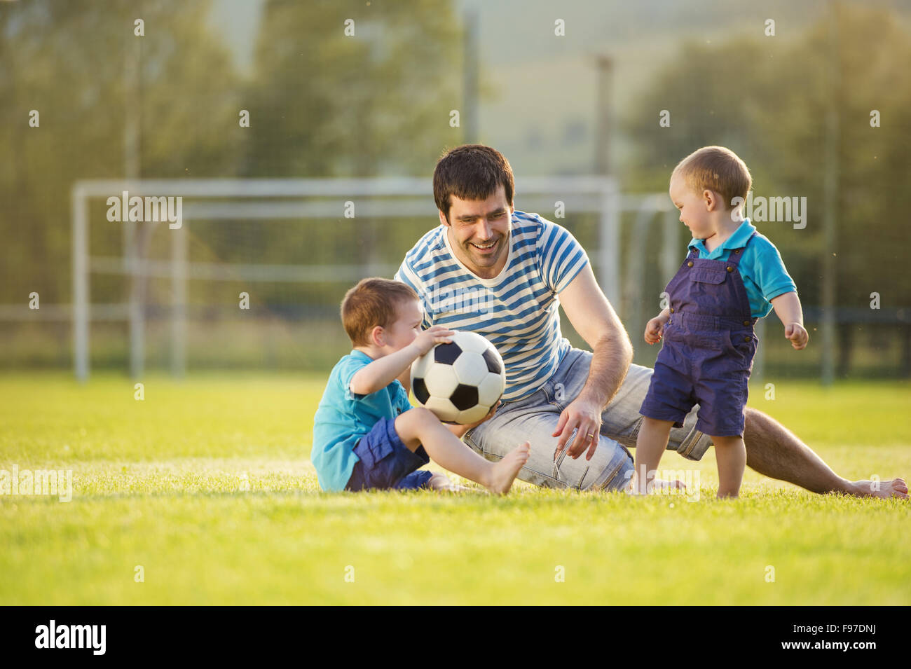 Young father with his little sons playing football on football pitch Stock Photo