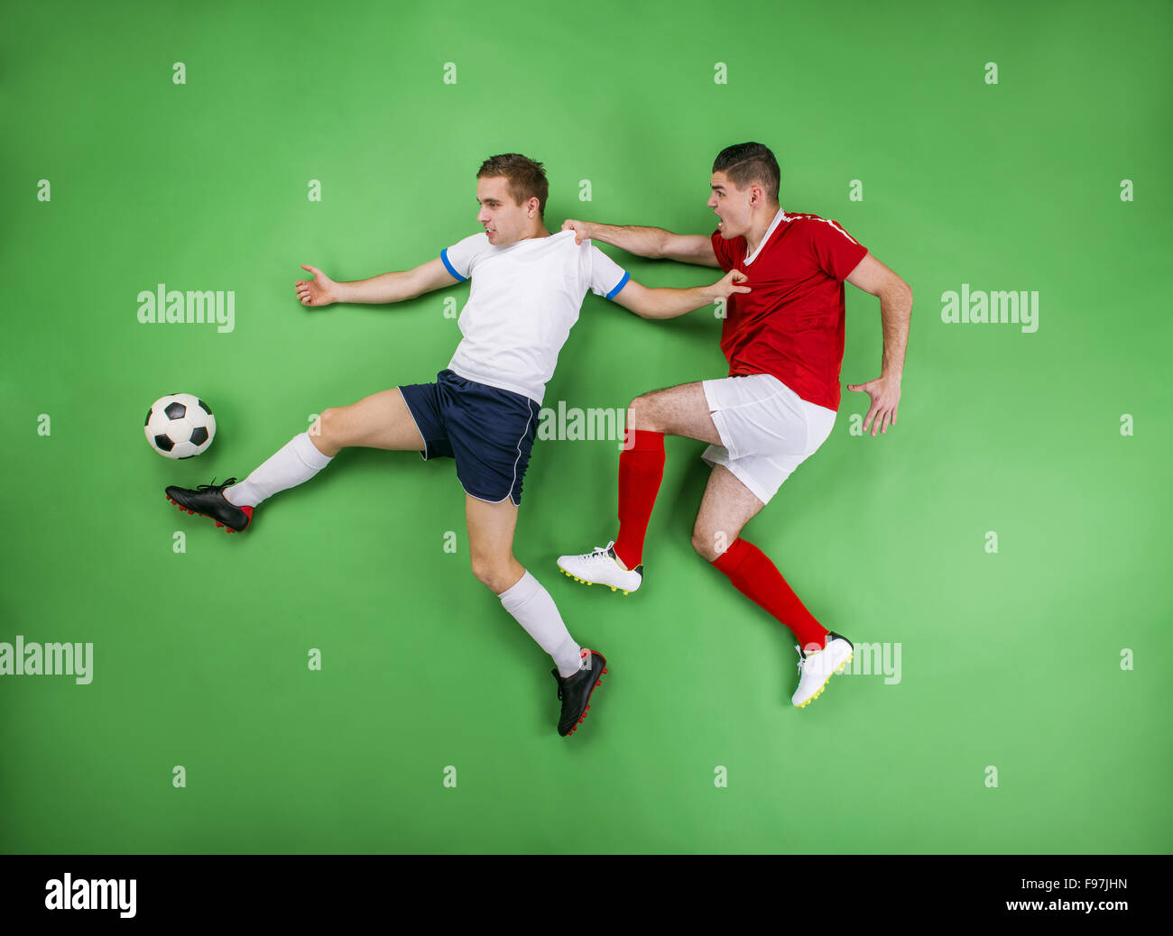 Two enthusiastic football players fighting for a ball. Studio shot on a green backgroud. Stock Photo