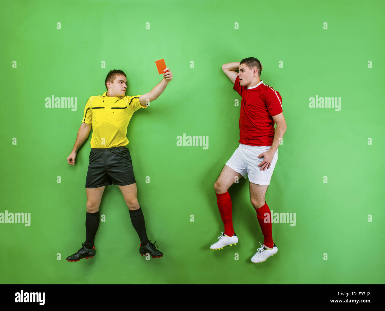 Referee giving red card to a football player. Studio shot on a green background. Stock Photo