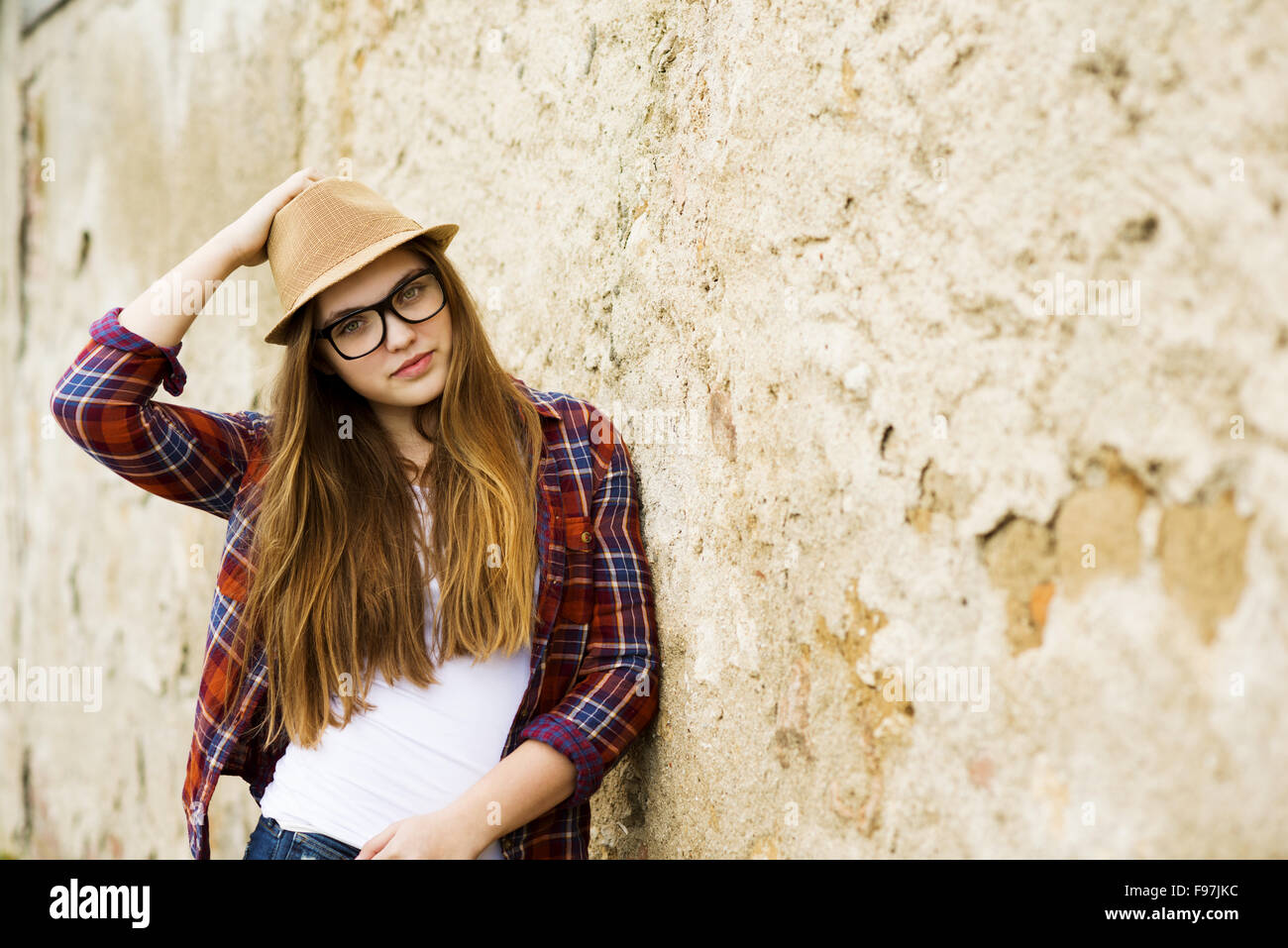 Outdoor portrait of teenage hipster girl in hat posing by the old wall Stock Photo