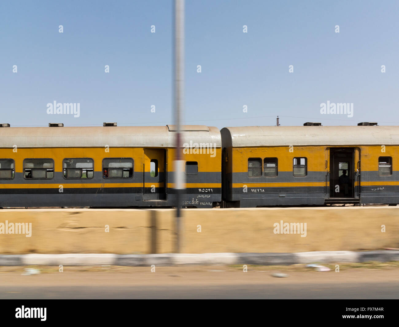 Train carriages passing at speed with movement blur on road and lamp post, Egypt, Africa Stock Photo