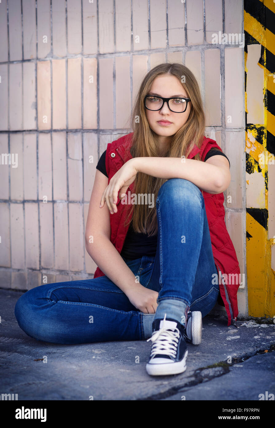 Sad teenage hipster girl sitting by the black and yellow striped warning wall Stock Photo