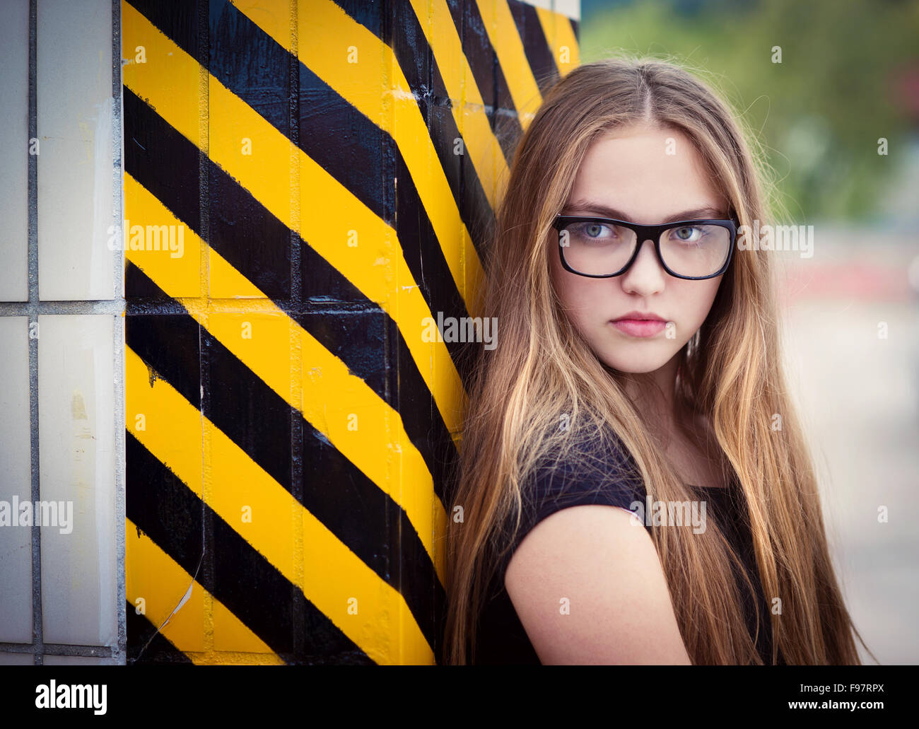 Portrait of sad teenage hipster girl standing by the black and yellow striped warning wall Stock Photo